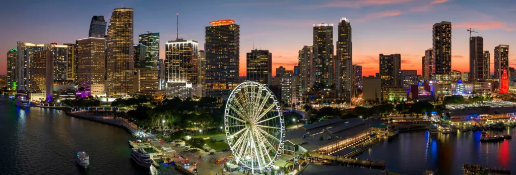 Miami skyline at sunset with Ferris wheel and waterfront.